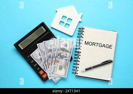 Word Mortgage écrit dans le carnet, la calculatrice et les dollars sur fond bleu clair, plat Banque D'Images