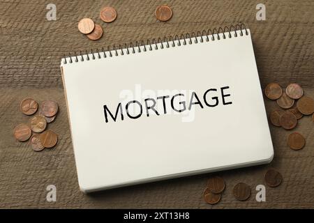 Word Mortgage écrit dans un cahier et des pièces de monnaie sur une table en bois, vue de dessus Banque D'Images