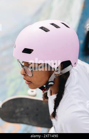 Jeune femme afro-américaine en lunettes portant un casque de protection lilas léger et patinant dans le parc Banque D'Images