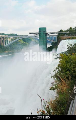 Cette image capture les chutes du Niagara à couper le souffle du côté américain, montrant les eaux brumeuses, une tour d'observation et un pont reliant le Canada Banque D'Images