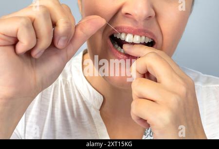 Image anonyme en gros plan d'une personne qui passe la soie dentaire, soulignant l'importance de la santé dentaire et des routines quotidiennes d'hygiène Banque D'Images