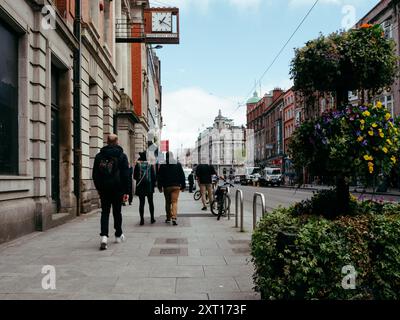 Une rue animée de la ville au printemps propose des piétons marchant le long du trottoir tandis que les cyclistes naviguent à proximité. Les gens habillés de façon décontractée s'engagent avec le Banque D'Images