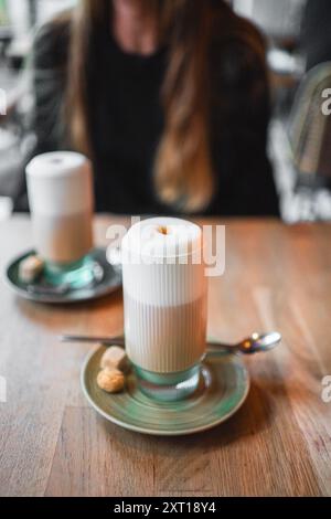 Délicieux café Latte Macchiato brun clair avec mousse de lait doux dans un beau verre côtelé avec des accents verts sur une assiette avec des biscuits debout sur un Banque D'Images