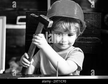 Un petit garçon avec un marteau fait des réparations. L'enfant participe activement au processus fait à la main. Banque D'Images