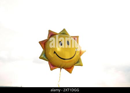 Un ballon d'hélium souriant en forme de soleil avec une couleur jaune vif flotte sur un fond de ciel lumineux. Bola02417 Copyright : xConnectxImagesx Banque D'Images