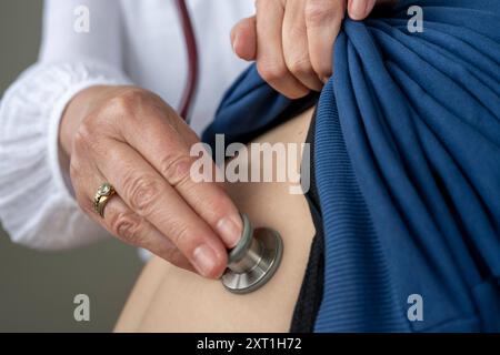Diverse situatie in een huisartsenpraktijk Un médecin effectue un examen physique en utilisant un stéthoscope sur le dos d un patient, soulevant une chemise bleue Banque D'Images
