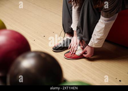 Attacher des chaussures de bowling tout en se préparant au jeu au bowling. Plancher en bois et boules de bowling colorées visibles en arrière-plan créant une atmosphère vibrante Banque D'Images