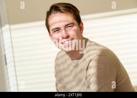 Portret van een jeune homme souriant millenial dans un pull beige posant à l'intérieur avec un fond lumineux. Molenhoek Nederland panc05374 Copyright : xConn Banque D'Images