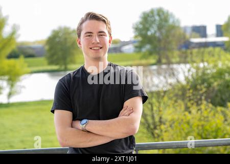 Portret van een jeune homme souriant millénaire avec les bras croisés debout à l'extérieur avec une végétation luxuriante et un plan d'eau en arrière-plan. Molenhoek ne Banque D'Images