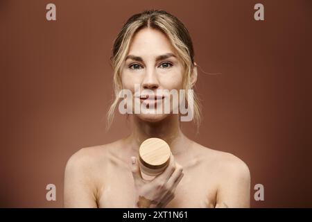 Une jeune femme atteinte de vitiligo tient un pot de crème devant un fond beige. Elle sourit et regarde directement la caméra. Banque D'Images