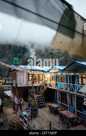 Tôt le matin dans un chalet de montagne rustique avec de la fumée qui s'élève d'une cheminée, des cabanes en bois colorées et des drapeaux de prière flottant dans la brise. Vietnam Banque D'Images