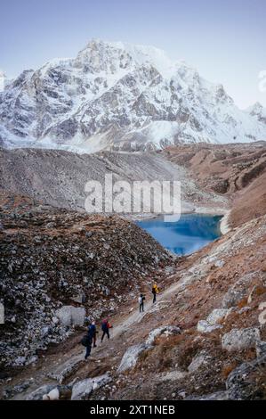 Les randonneurs marchent le long d'un sentier de montagne à côté d'un lac alpin bleu profond avec des pics accidentés couverts de neige en arrière-plan. Vietnam rist00076 Copyright : xConne Banque D'Images