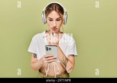 Une jeune femme dans une tenue d'été blanche pose sur un fond vert, regardant soigneusement son téléphone. Banque D'Images