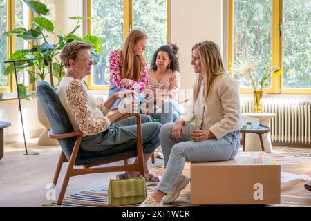 Quatre femmes de différents âges profitant d'une conversation décontractée dans un salon ensoleillé, avec de grandes fenêtres et une végétation luxuriante à l'extérieur. Panc05635 Copyright : x Banque D'Images