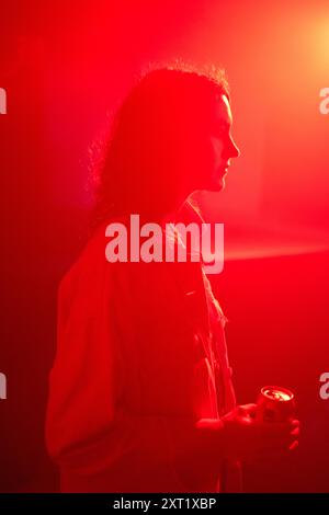 Vue de profil d'une femme debout dans un éclairage ambiant rouge tenant une boîte. Bola02625 Copyright : xConnectxImagesx Banque D'Images