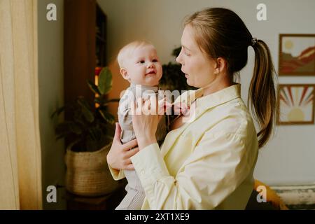 Mère souriante tenant bébé dans la chambre ensoleillée Banque D'Images