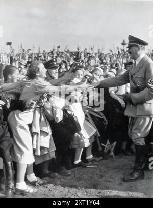 Une photographie montre des partisans enthousiastes rencontrant Adolf Hitler, reflétant la dévotion orchestrée que le régime nazi cultivait parmi la population allemande. De telles démonstrations de loyauté étaient essentielles pour maintenir l’autorité d’Hitler et faire avancer le programme du régime. Banque D'Images