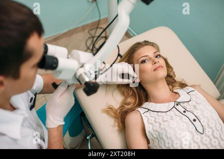 Un clinicien examine soigneusement l'oreille d'un patient à l'aide d'un microscope dans un cabinet médical lumineux et propre. Banque D'Images