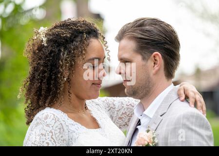 Moment intime entre une mariée en robe de dentelle et un marié en costume gris, partageant un regard sur un fond naturel flou. Panc05793 Copyright : xc Banque D'Images