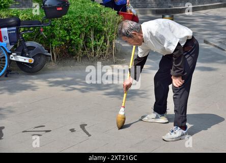 Homme pratiquant la calligraphie de l'eau (écriture au sol - dishu), passe-temps populaire parmi les Chinois retraités, à Pékin, Chine le 21 avril 2024 Banque D'Images