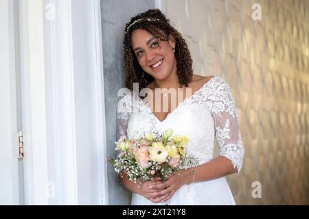 Mariée souriante tenant un bouquet se tient près d'une porte, exsudant le bonheur le jour de son mariage. Panc05961 Copyright : xConnectxImagesx Banque D'Images