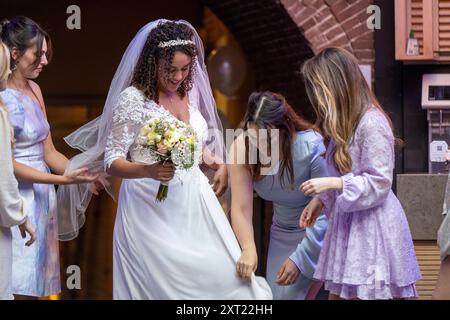 Mariée dans une robe blanche avec un voile et un bouquet est aidé par trois demoiselles d'honneur en robes bleues et violettes dans une rue de la ville. Panc05996 Copyright : Banque D'Images