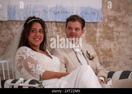 Mariée et mariée souriant assis à leur mariage, avec la mariée dans une robe de dentelle et le marié dans un costume beige. Panc06011 Copyright : xConnectxIma Banque D'Images