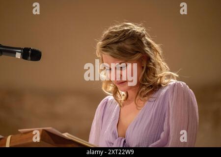 Une femme dans une blouse violette lit depuis un podium avec un microphone dans une pièce légèrement éclairée. Panc06021 Copyright : xConnectxImagesx Banque D'Images