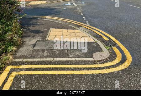 Doubles lignes jaunes peintes à un angle inhabituel autour d'un coin. Banque D'Images