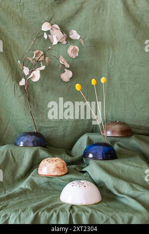 Arrangement artistique de porte-fleurs en céramique avec des fleurs séchées sur un fond de tissu vert Banque D'Images