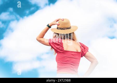 Blonde jeune femme caucasienne en blouse rouge et chapeau de paille parmi les nuages d'en bas Banque D'Images