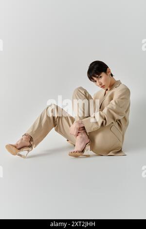 Une femme en costume beige est assise avec les jambes croisées, sur un fond blanc. Banque D'Images