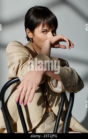 Une femme portant un blazer bronzé pose dans un studio avec un fond ensoleillé. Banque D'Images