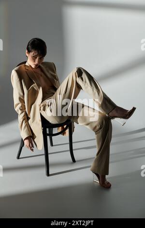 Une femme en costume beige est assise sur une chaise sur un fond blanc. Banque D'Images