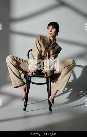 Une femme en costume beige est assise sur une chaise, les jambes étendues, posant pour une séance photo. Banque D'Images