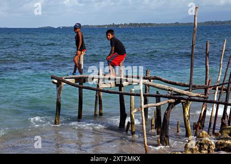 Kuna Boy stting sur la jetée rustique faite de poteaux en bois, bâtons et poutres, Carti Sugtup Island, San Blas Islands, Panama Banque D'Images