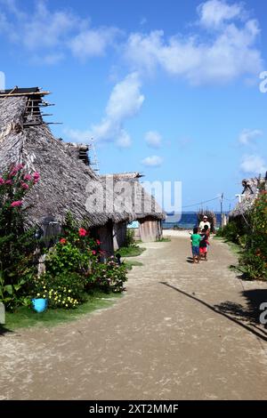 Famille Kuna dans la rue bordée de bambou typiques et feuilles de palmier chaume huttes et fleurs tropicales, Carti Yandup Island, San Blas Islands, Panama Banque D'Images