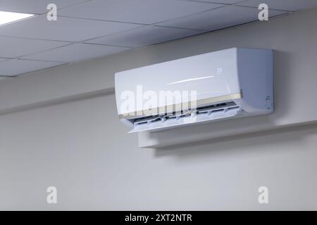Gros plan d'un climatiseur mural dans une pièce avec un plafond carrelé, mettant en évidence la technologie moderne de contrôle du climat. Banque D'Images