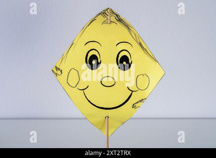 Une émoticône souriante sur un morceau de papier jaune percé d'un bâton de bois Banque D'Images