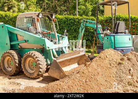 Un travailleur sur un chargeur de peau déplace la terre, excavée devant la maison. Travaux d'excavation et pavage extérieur. Banque D'Images