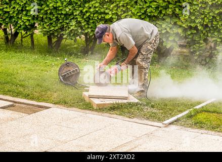 Ouvrier coupant des dalles de béton pour le sol avec scie électrique circulaire. Banque D'Images