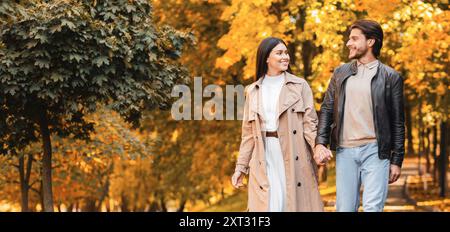 Homme et femme positifs se tenant les mains et marchant au parc Banque D'Images