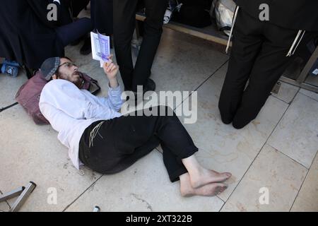 Juif orthodoxe pieds nus avec un yarmulka se trouve sur le sol lit Lamentations & prières au mur occidental le jour de la destruction du Temple Tisha B'AV. Banque D'Images