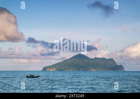 Un paysage côtier serein avec Turtle Island à l'horizon. L'île est encadrée par une vaste étendue d'océan bleu et un ciel orné de peluches Banque D'Images