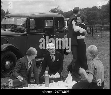 Civils hommes et femmes pique-niquant à côté d'une voiture pendant que deux d'entre eux dansent, 1931. « S'éloigner de tout cela était... une autre caractéristique de l'époque. En voiture, en pédalant ou à pied, les masses cherchaient l'air frais, comme si cela aussi était quelque chose qui venait d'être inventé. De "Time to Remember - A New Era", 1931 (Reel 2) ; documentaire sur le monde au début des années 1930 Banque D'Images