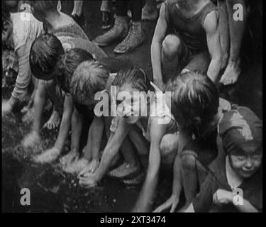 Enfants éclaboussant dans l'eau dans la gouttière pendant une canicule à New York, 1921. De "Time to Remember - The Time When Little Happen", 1921 (bobine 3) ; événements de 1921 - traité irlandais, cascades folles et journaux au travail. Banque D'Images