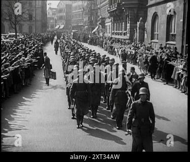 Foule regardant des soldats allemands marcher dans une rue vers la caméra, années 1930 De "Time to Remember - The Powers That Were", années 1930 (Reel 3) ; un documentaire sur diverses figures importantes des années 1930 Banque D'Images