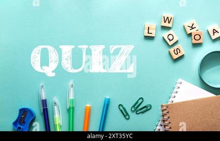 Un fond vert et bleu avec un mot blanc quiz écrit en blanc. Il y a plusieurs stylos et crayons sur la table, et une pile de livres Banque D'Images