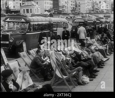 Hommes et femmes assis dans des transats sur la Promenade à Brighton avec une rangée de bus derrière eux sur la route et les bâtiments de Marine Parade visible derrière, 1939. De "Time to Remember - The Reluctant Warriors", 1939 (bobine 1) ; documentaire sur les événements de 1939 - les préparatifs de la guerre et les hostilités éclatent. Banque D'Images
