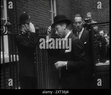 Un officier de police britannique saluant le roi George VI, le monarque britannique qui sort d'une voiture avec la porte tenue ouverte par un membre masculin de son personnel et enlevant son chapeau Bowler alors qu'il marche d'une voiture à la porte du numéro dix Downing Street tandis qu'un groupe de photographes sont debout derrière, 1939. De "Time to Remember - The Reluctant Warriors", 1939 ( Reel 2) ; documentaire sur les événements de 1939 - les préparatifs pour la guerre et les hostilités éclatent. Banque D'Images
